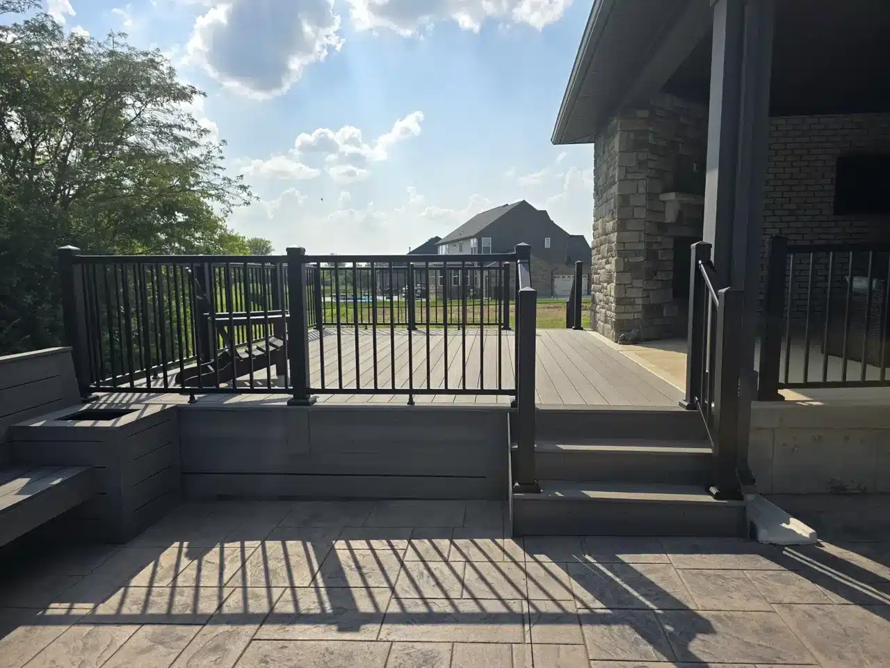 A custom composite deck with a geometric design featuring built-in seating, adjacent to a small outdoor shed with a grill area