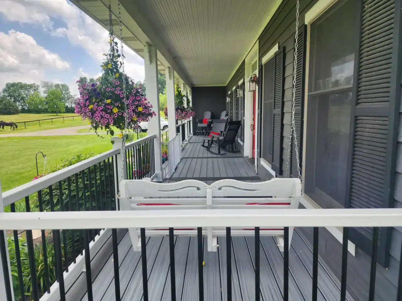 A front porch with a wooden bench and hanging flower baskets, featuring a railing and grey composite decking.
