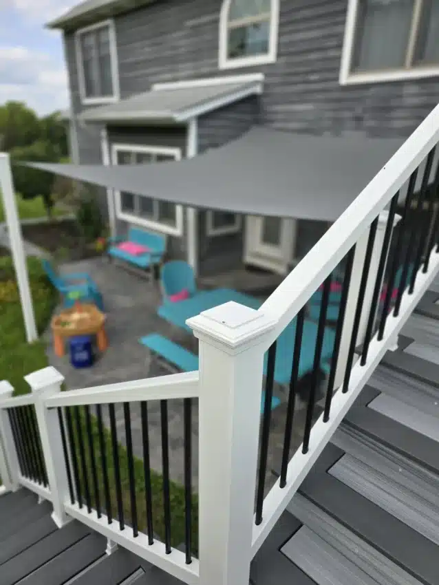Close-up of white and black composite deck railing overlooking a shaded backyard patio with seating