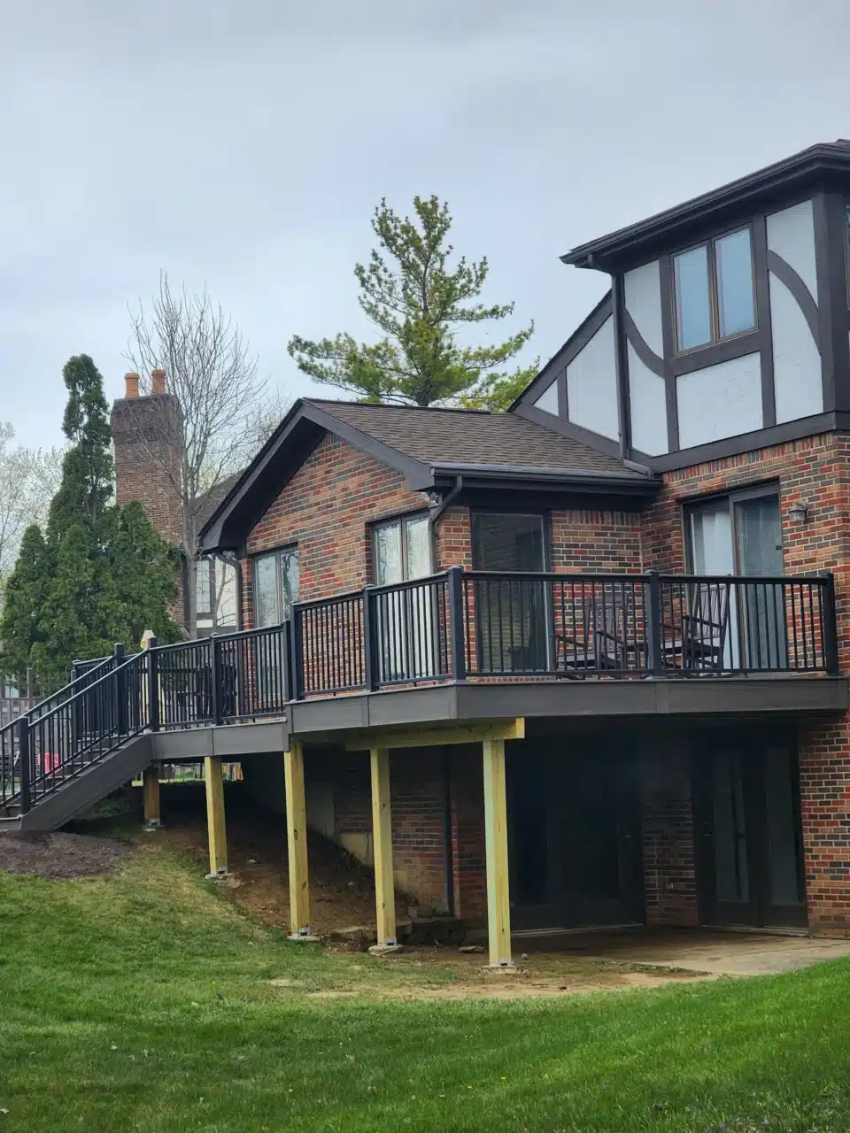 View from the front-left of a raised deck with black railing, attached to a brick house. The staircase leads down to the yard.