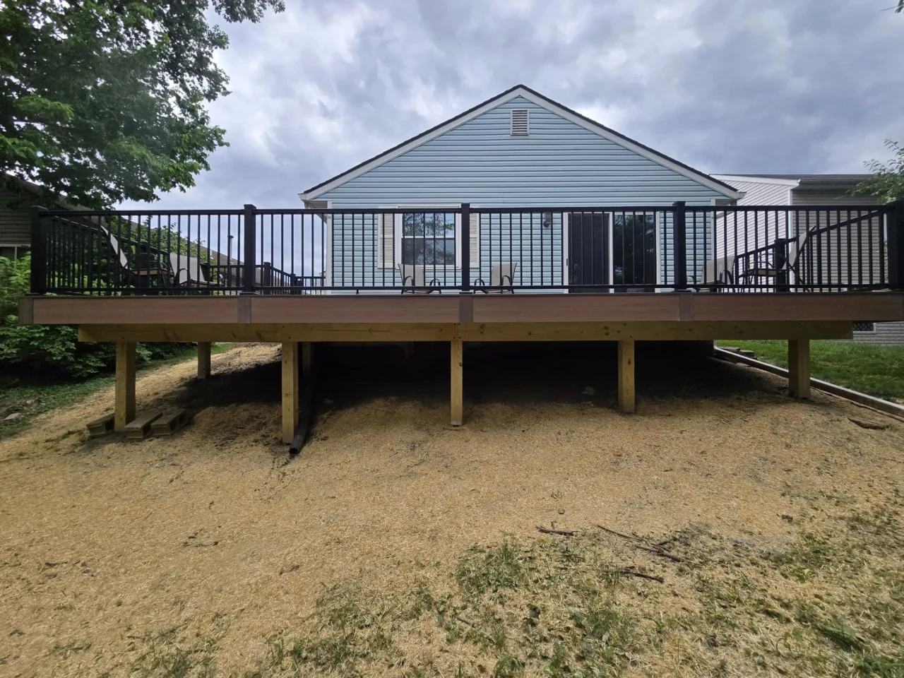 View of the deck from the ground level, showing the black aluminum railing, the understructure of the deck, and the back of the house with chairs on the deck.