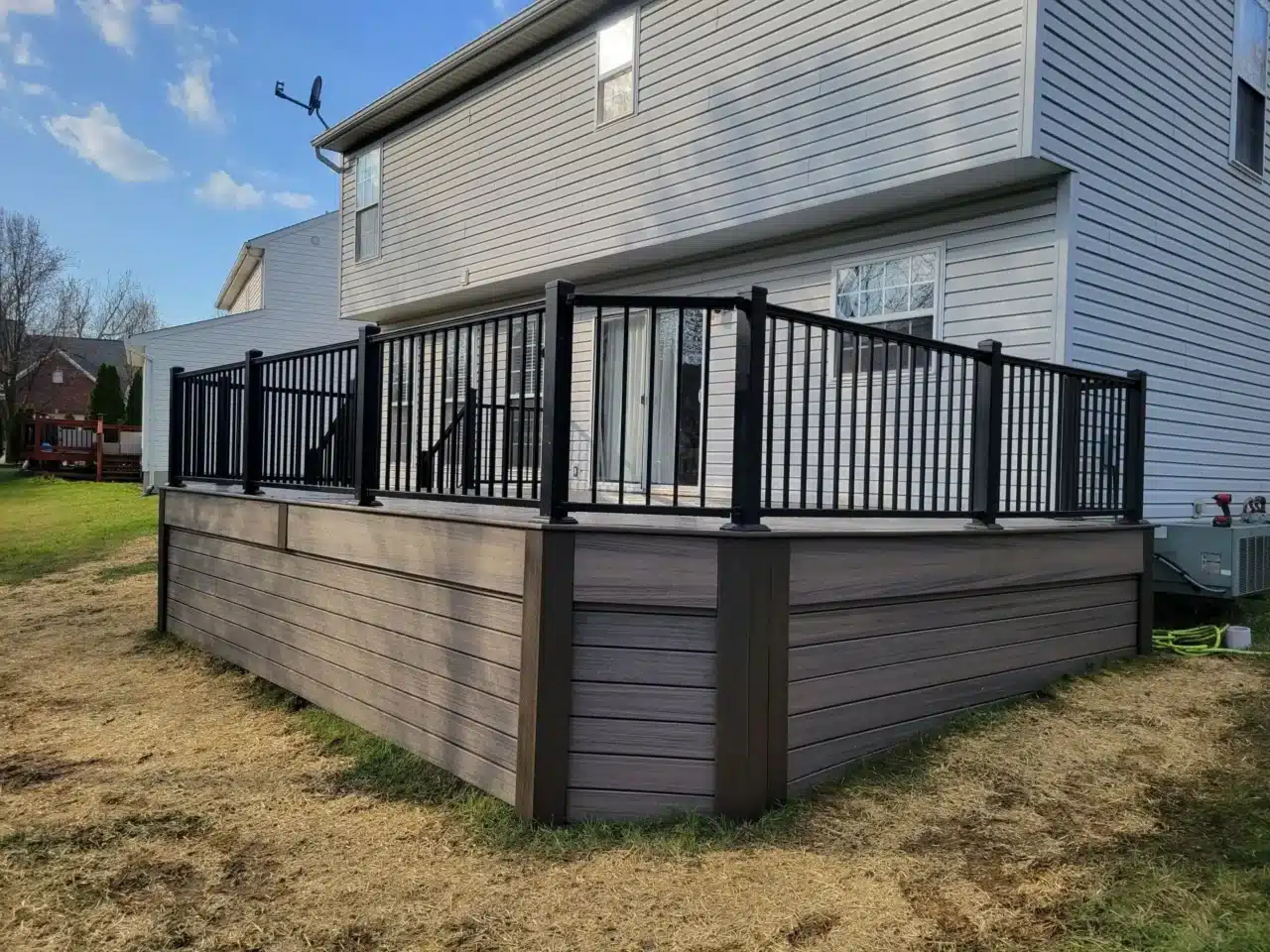 Composite deck with black railings by top deck builder in Mason A large deck with dark composite decking and black metal railings at the back of a house.