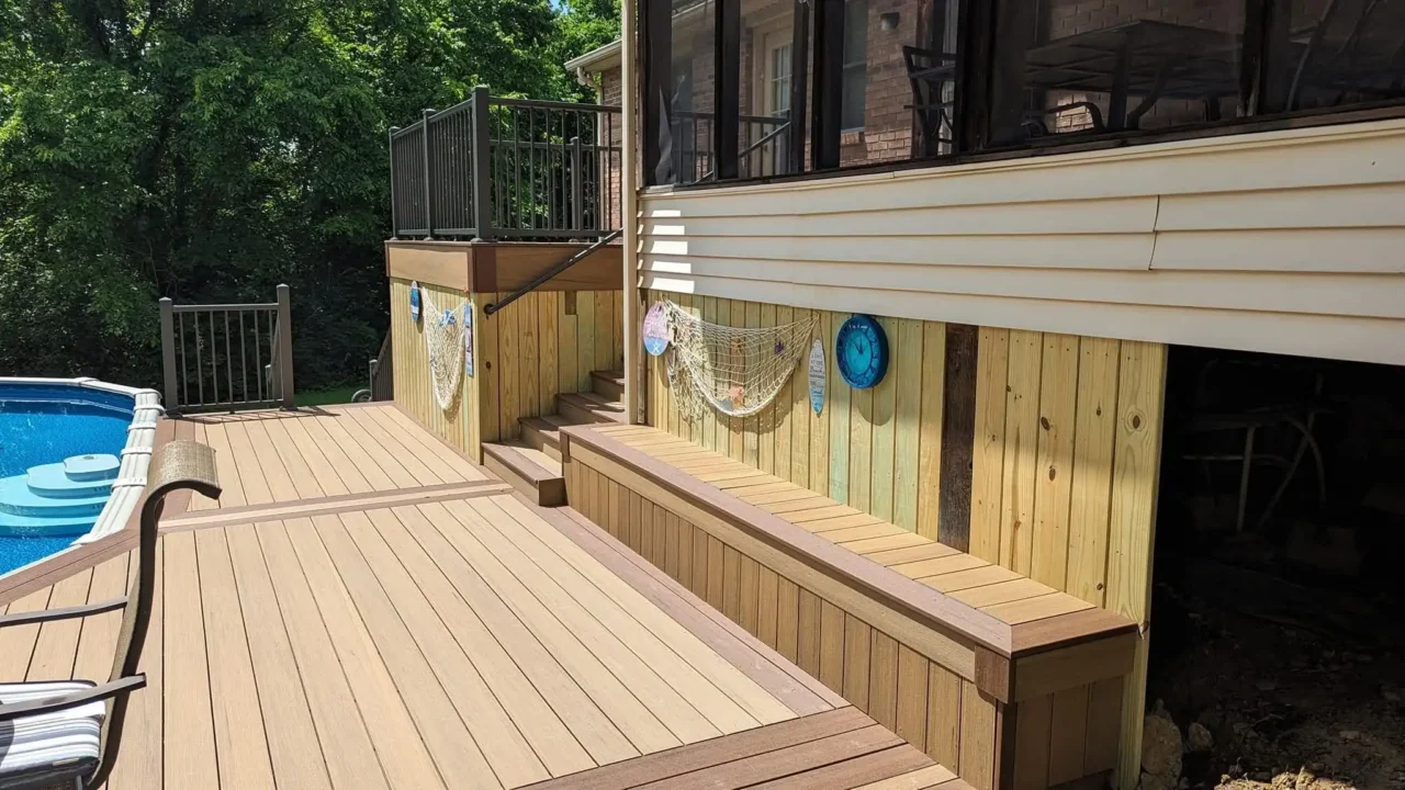 View of the pool deck showing TimberTech Terrain composite decking, built-in bench seating, and the skirting decorated with fishing nets. The upper deck with black aluminum railing is visible in the background.