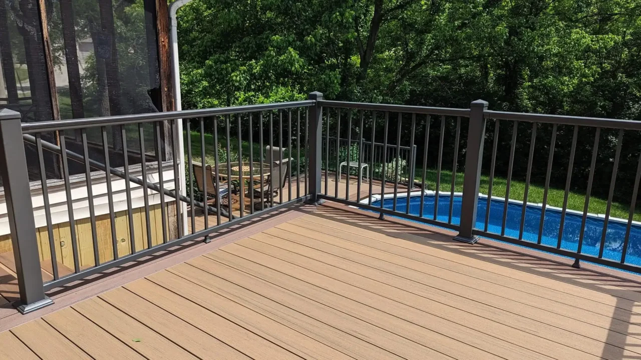 Close-up view of the upper deck with TimberTech Terrain composite decking and black aluminum railing. The pool and additional seating area are visible in the background.